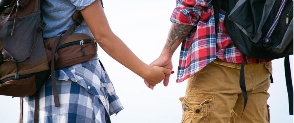 Couple holding hands while walking with backpacks